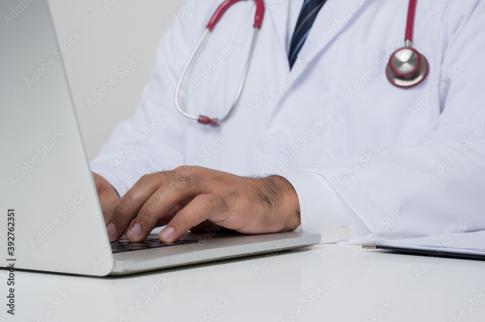 Close up of Asian doctor put on stethoscope working on laptop sitting at the desk isolated on white background. Close up of Asian doctor put on stethoscope working on laptop sitting at the desk isolated on white background.