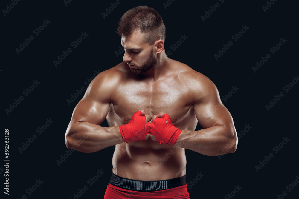 Front view of a sporty man in boxing gloves practicing fighting techniques isolated on black background Front view of a sporty man in boxing gloves practicing fighting techniques isolated on black background