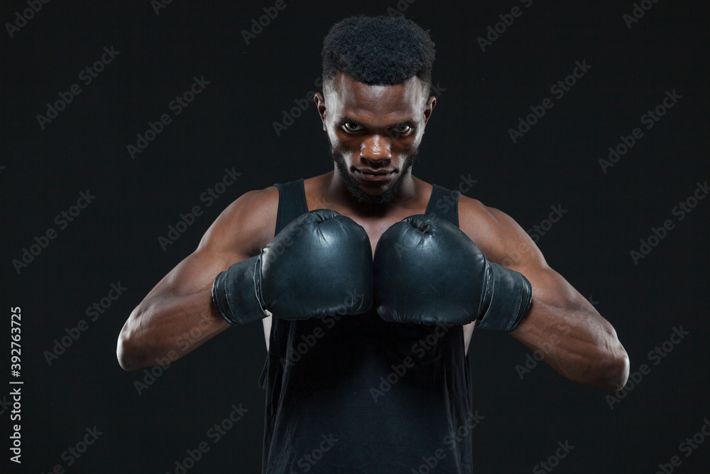 Front view shot of young African American boxer wearing gloves is posing isolated on a dark background