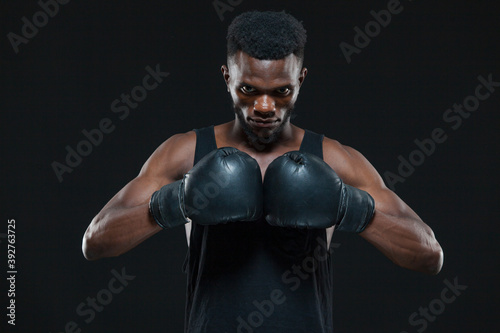 Front view shot of young African American boxer wearing gloves is posing isolated on a dark background © satyrenko