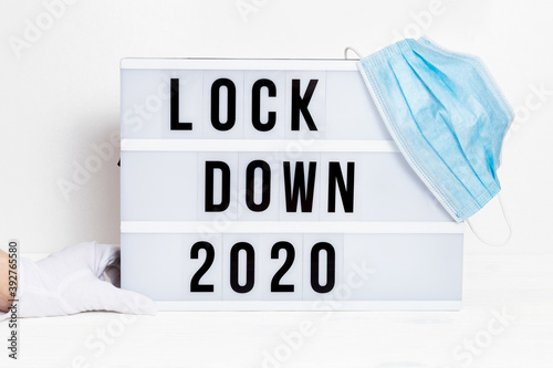 Hands in white gloves hold Light box with message lockdown 2020 and Surgical protective mask. Word of the Year 2020 is lockdown. photo