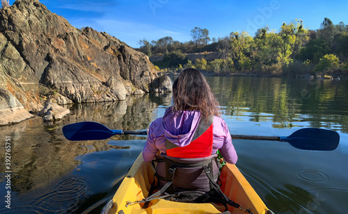 Back view middle age woman holding paddle in double kayak looking at beautiful river view 