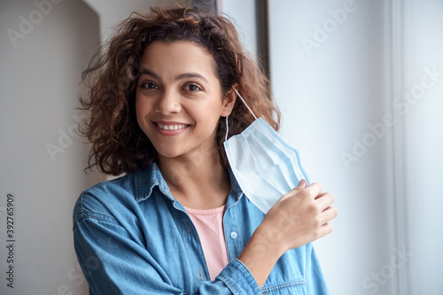 Quadro em tela Happy Hispanic young woman takes off protective mask indoors.