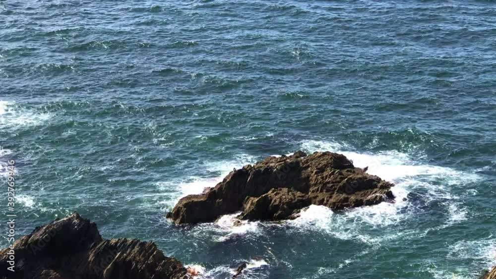 Rugged rock formation emerging from harsh ocean crashing tide waves Rugged rock formation emerging from harsh ocean crashing tide waves