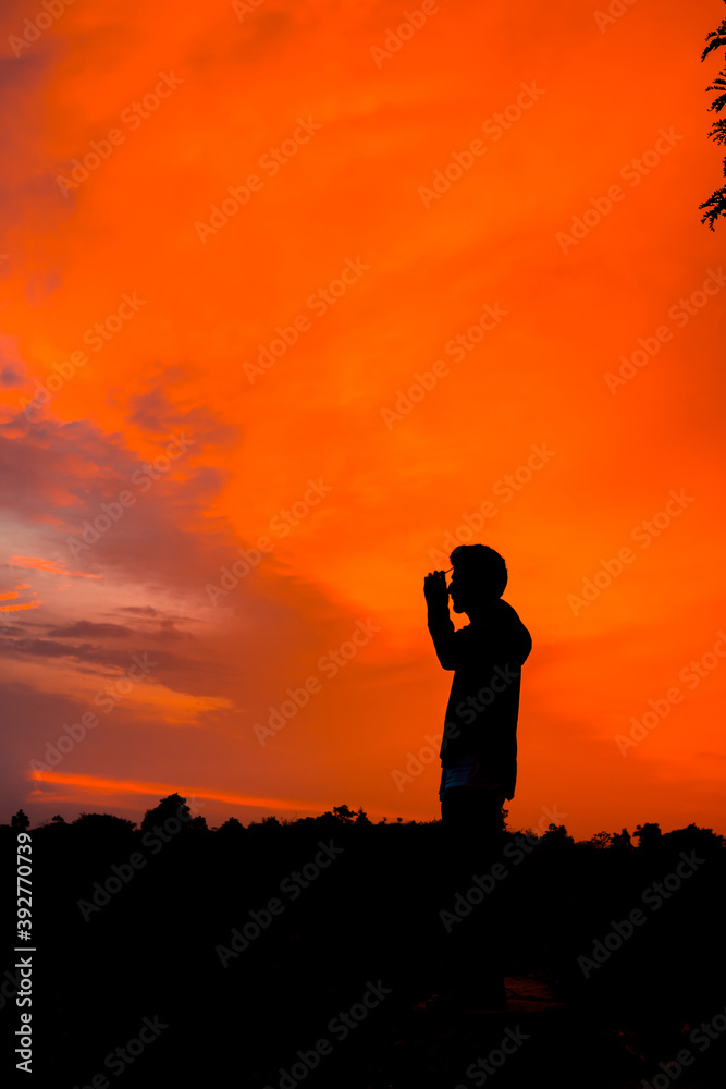 Silhouette of lonely person standing in front of sunset by wearing glasses