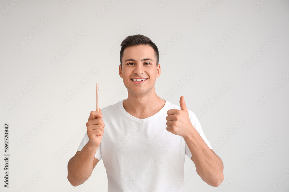 Young man with tooth brush showing thumb-up on light background Young man with tooth brush showing thumb-up on light background