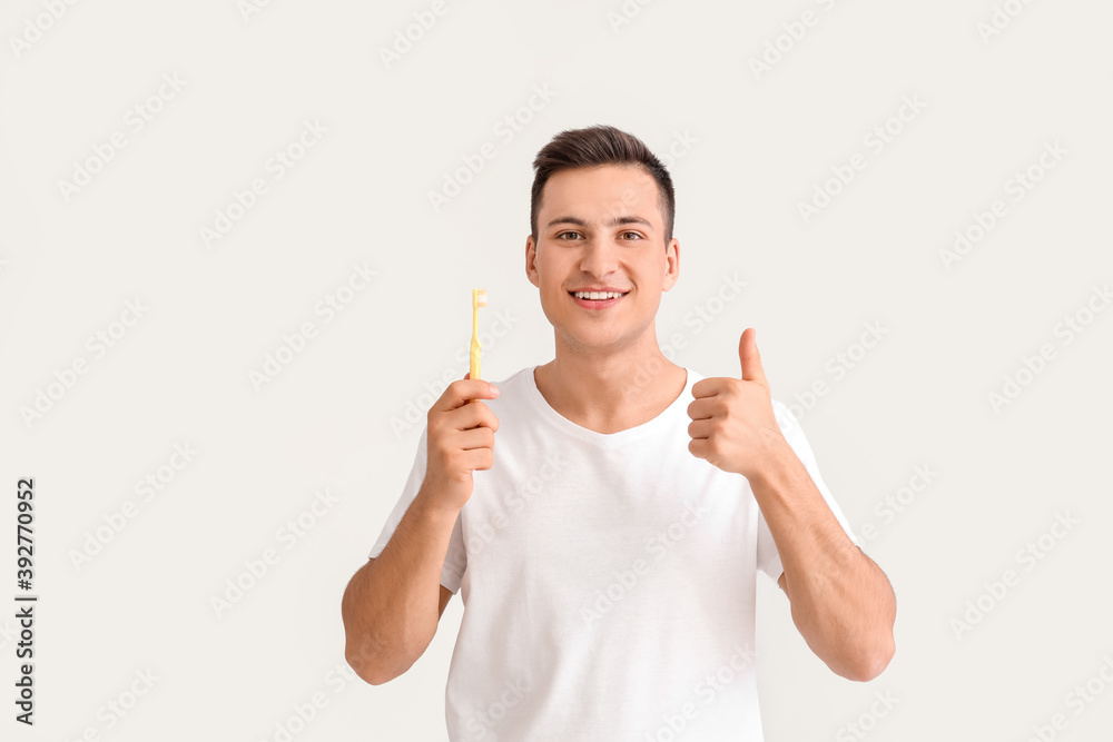 Young man with tooth brush showing thumb-up on light background Young man with tooth brush showing thumb-up on light background