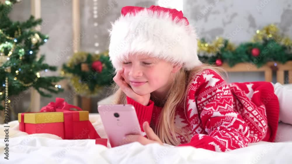 4k Christmas online congratulations. Smiling girl using mobile phone for video call. Child talking friends and parents. 4k Christmas online congratulations. Smiling girl using mobile phone for video call. Child talking friends and parents.