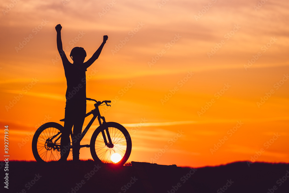 Fototapeta premium Silhouette of a mountain biker at sunset with arms raised