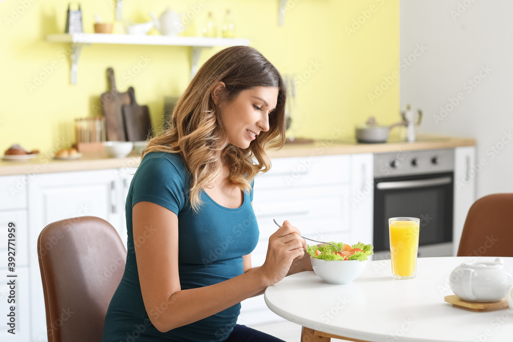 Beautiful pregnant woman eating healthy vegetable salad in kitchen Beautiful pregnant woman eating healthy vegetable salad in kitchen