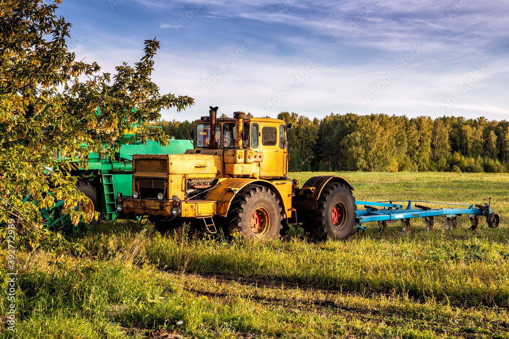 Obraz premium Wheeled agricultural tractor with harvesting equipment on an field