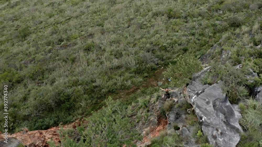 Female rock climber ascending rock face, aerial reveal surrounding landscape Female rock climber ascending rock face, aerial reveal surrounding landscape