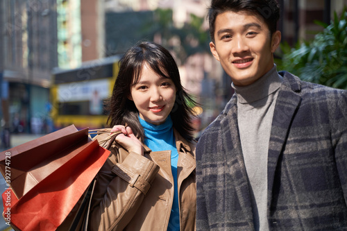outdoor portrait of young asian couple holding shopping bags