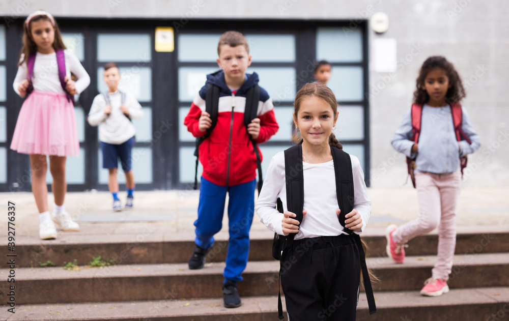 Fototapeta premium Portrait of smiling schoolgirl standing on the street, kids on background
