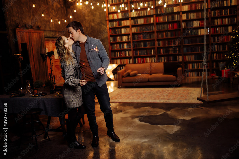 Beautiful couple kissing, hold sparklers in arms, adorable wife and charming husband enjoy festive mood, cozy winter holidays at home, New Year and Christmas celebration concept