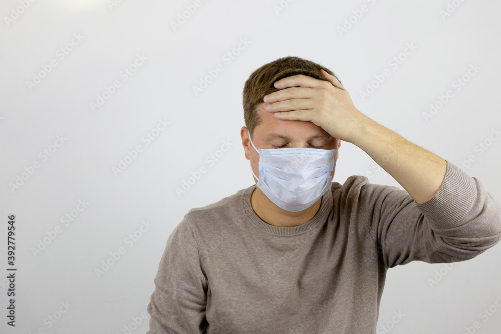 A man in a medical mask suffers from malaise and holds on to his forehead with one hand. Fever, malaise, mild cough. A man in a medical mask suffers from malaise and holds on to his forehead with one hand. Fever, malaise, mild cough.