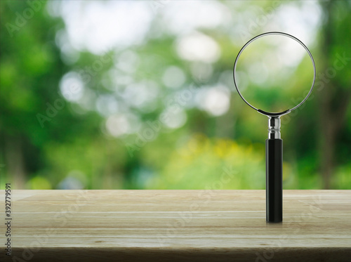 Magnifying glass on wooden table over blur green tree in park, Business analyzing concept