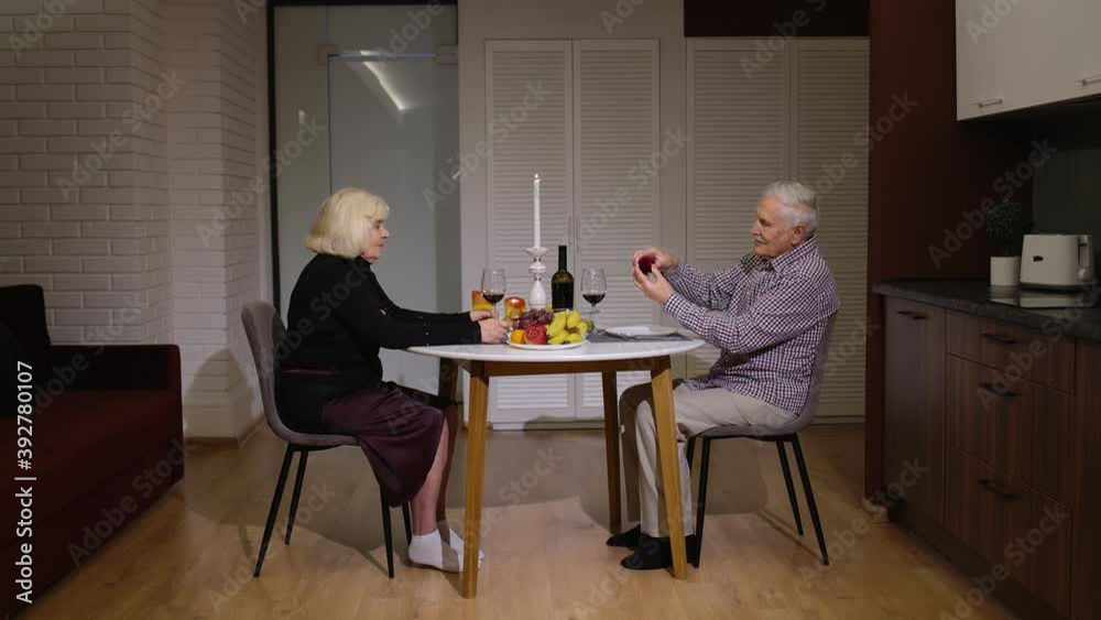 Senior man asking for marriage his grandmother girlfriend. Grandfather making proposal to his bride fiancee to be in kitchen during romantic dinner. Happy surprised woman smiling being speechless Senior man asking for marriage his grandmother girlfriend. Grandfather making proposal to his bride fiancee to be in kitchen during romantic dinner. Happy surprised woman smiling being speechless