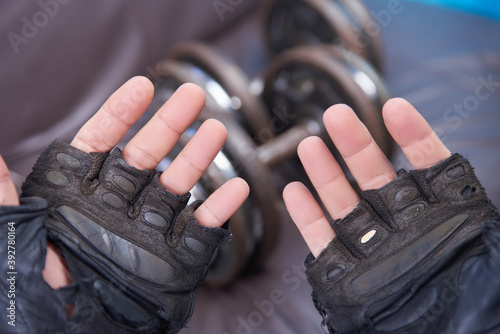 Hands wearing Old worn gloves in the foreground  rusty dumbbells 