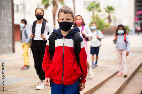 Confident tweenager in protective mask walking with other schoolchildren to school campus after lessons on spring day. Concept of necessary precautions in COVID pandemic