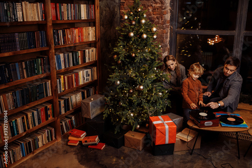 Joyful parents with little son near Christmas tree, happy family listening music plates, smiling, enjoy festive mood, vinyl music, winter holidays at home, xmas concept