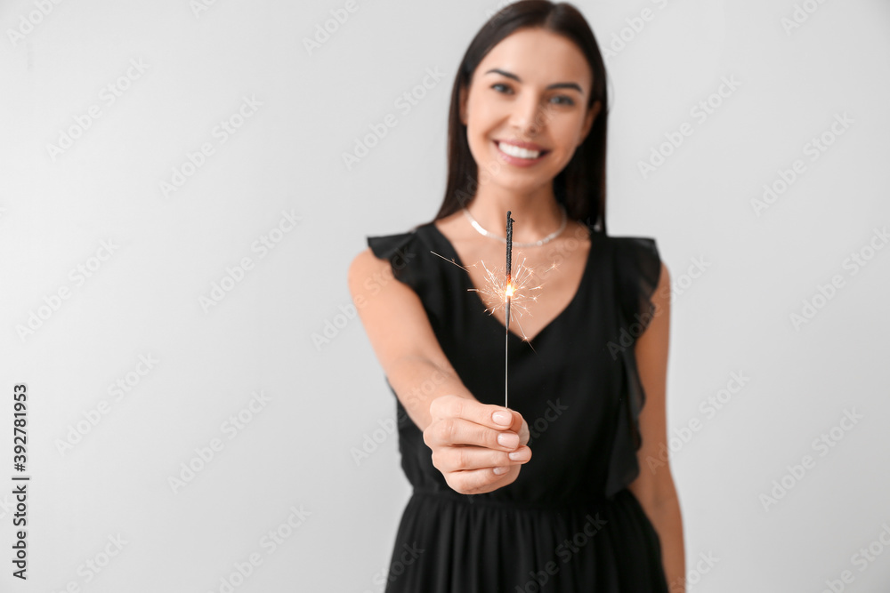 Beautiful young woman with Christmas sparklers on light background Beautiful young woman with Christmas sparklers on light background