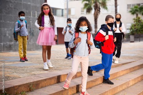 Tween schoolchildren in protective masks with backpacks going to school lessons on autumn day. Back school concept during pandemic