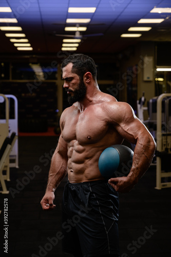 strong caucasian male with beard holding heavy medicine ball in sport fitness gym