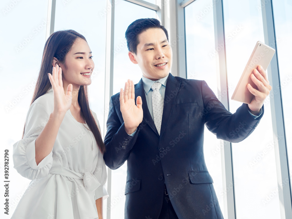 Asian businessman in suit and young woman making video call with digital tablet on glass window background. Asian businessman in suit and young woman making video call with digital tablet on glass window background.