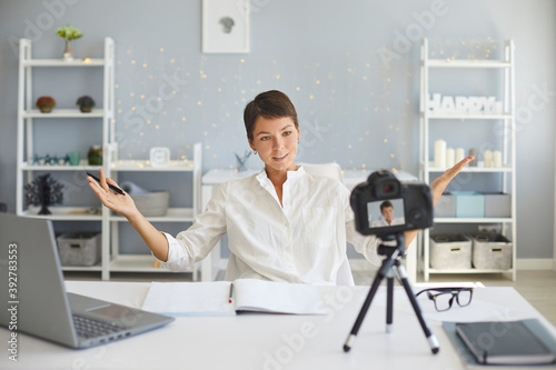 Confident female vlogger recording video on camera sitting at her desk in cozy home office photo