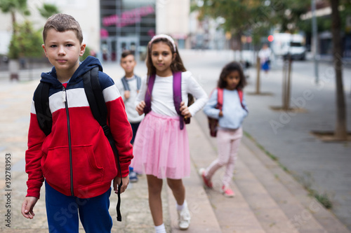 Portrait of positive boy standing near school, children on background