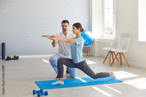 Man chiropractor fixing woman patients movements during exercising on fitness mat
