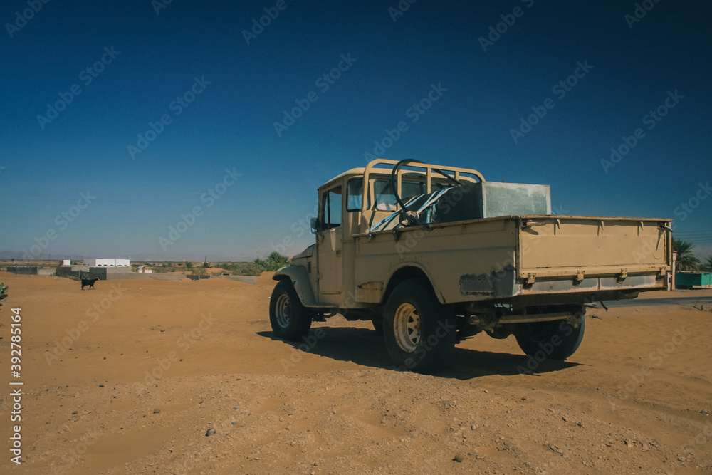 An old jeep standing peacefully on a flat part of a sand dune, close to oasis. Typical arab transporter.