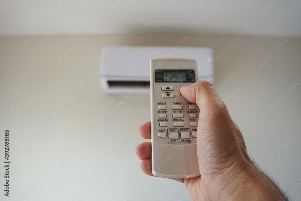 Turn on the air conditioner at 25 degrees Celsius. Hand holding the air conditioner remote control and thumb is pressing a button on the remote.