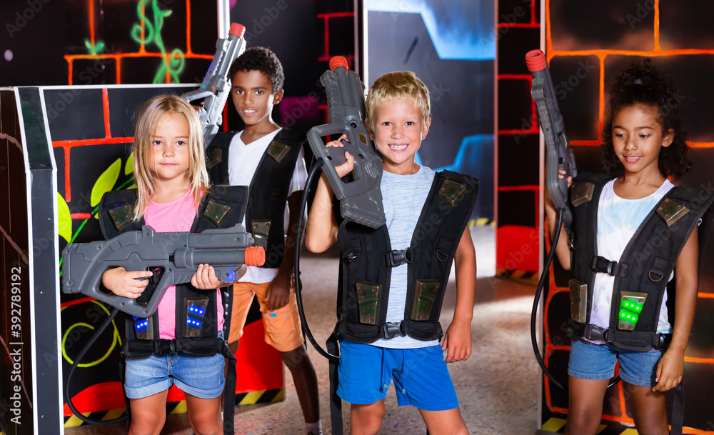Cheerful tween girls and boys of different nationalities with a laser pistols posing together in a dark laser tag labyrinth