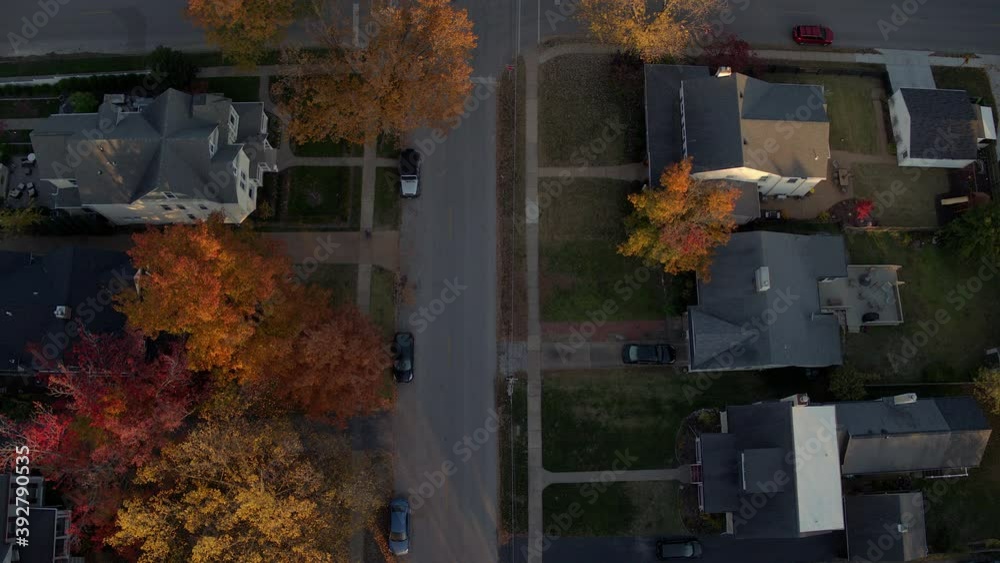 Aerial pulling back and tilting up over a beautiful street in a Kirkwood neighborhood in St. Louis, Missouri in Fall at peak color on a pretty evening at golden hour.