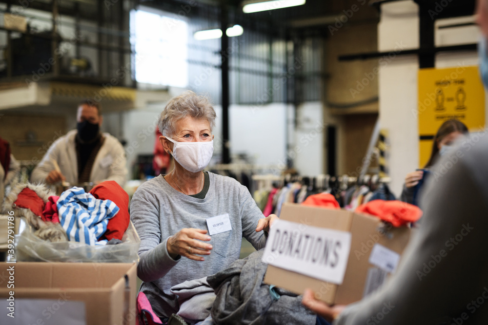 Volunteers sorting out donated clothes in community charity donation center, coronavirus concept. Volunteers sorting out donated clothes in community charity donation center, coronavirus concept.