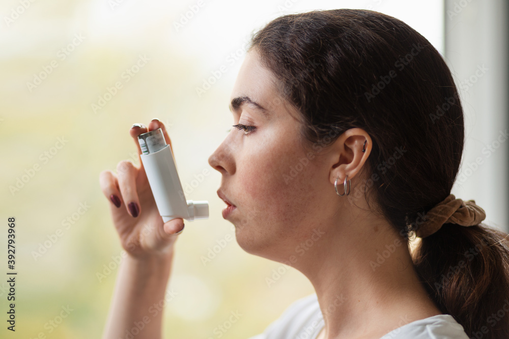 Close-up portrait of a young woman holding an inhaler to her mouth. Side view Close-up portrait of a young woman holding an inhaler to her mouth. Side view