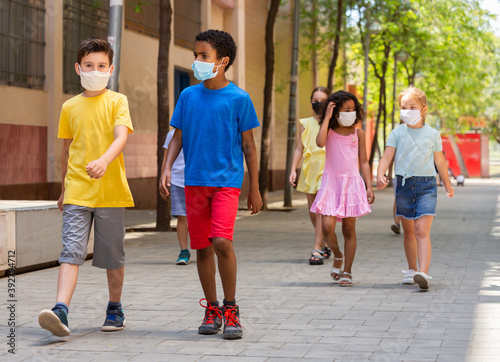 Schoolchildren in masks walking together on the street from school