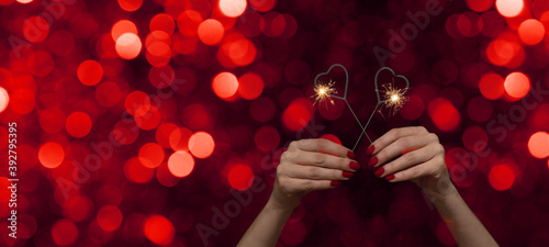 Valentine's Day /Love /Wedding / Birthday / Silvester / New Year / Party background - happy woman holding an sparkling heart sparklers in her hands, with red nails at night with red bokeh lights photo