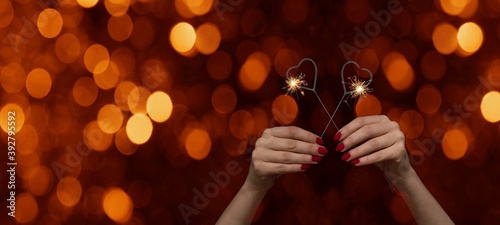 Valentine s Day  Love  Wedding   Birthday   Silvester   New Year   Party background banner - Happy woman holding sparkling heart sparklers in her hands  with red nails at black night and orange bokeh