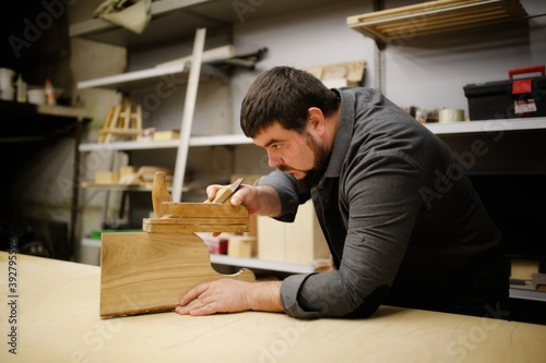 Bearded kraft caucasian man working with hand plane with cutting board made of handmade wood in workshop, handcraft and craftsmanship concept