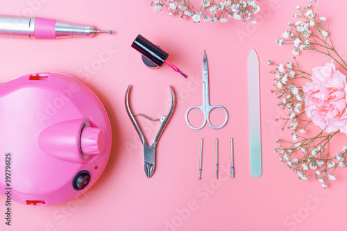 Manicure tools and drill on pink background, top view.