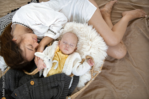 Mom and baby are sleeping. Little boy in a wicker cradle with a toy on the background of a blanket. Happy family concept.