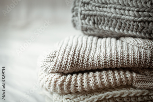 A stack of warm knitted items on blurred white background close up.