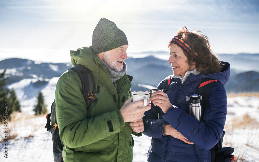 Senior couple hikers in snow-covered winter nature, drinking hot tea.