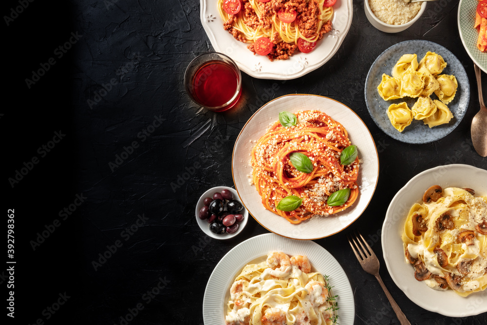 Italian food, overhead flat lay shot. Pasta, olives, wine on a black background with copy space. Spaghetti with tomato sauce, ravioli, and other classic dishes Italian food, overhead flat lay shot. Pasta, olives, wine on a black background with copy space. Spaghetti with tomato sauce, ravioli, and other classic dishes