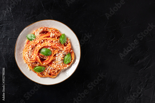 Tomato spaghetti. Pasta with red sauce, grated Parmesan cheese and fresh basil, shot from the top on a dark background with copyspace