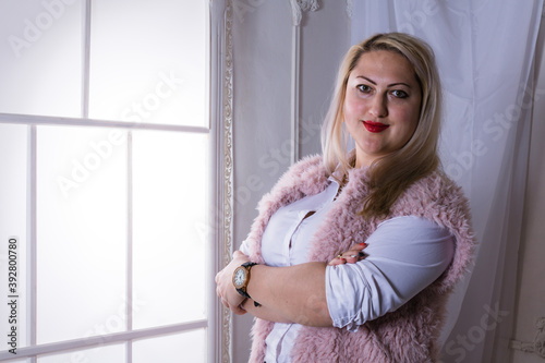 Attractive plump woman standing near window studio portrait. photo