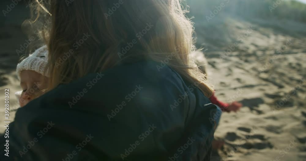 A young mother is watching her preschooler play on the beach in autumn A young mother is watching her preschooler play on the beach in autumn